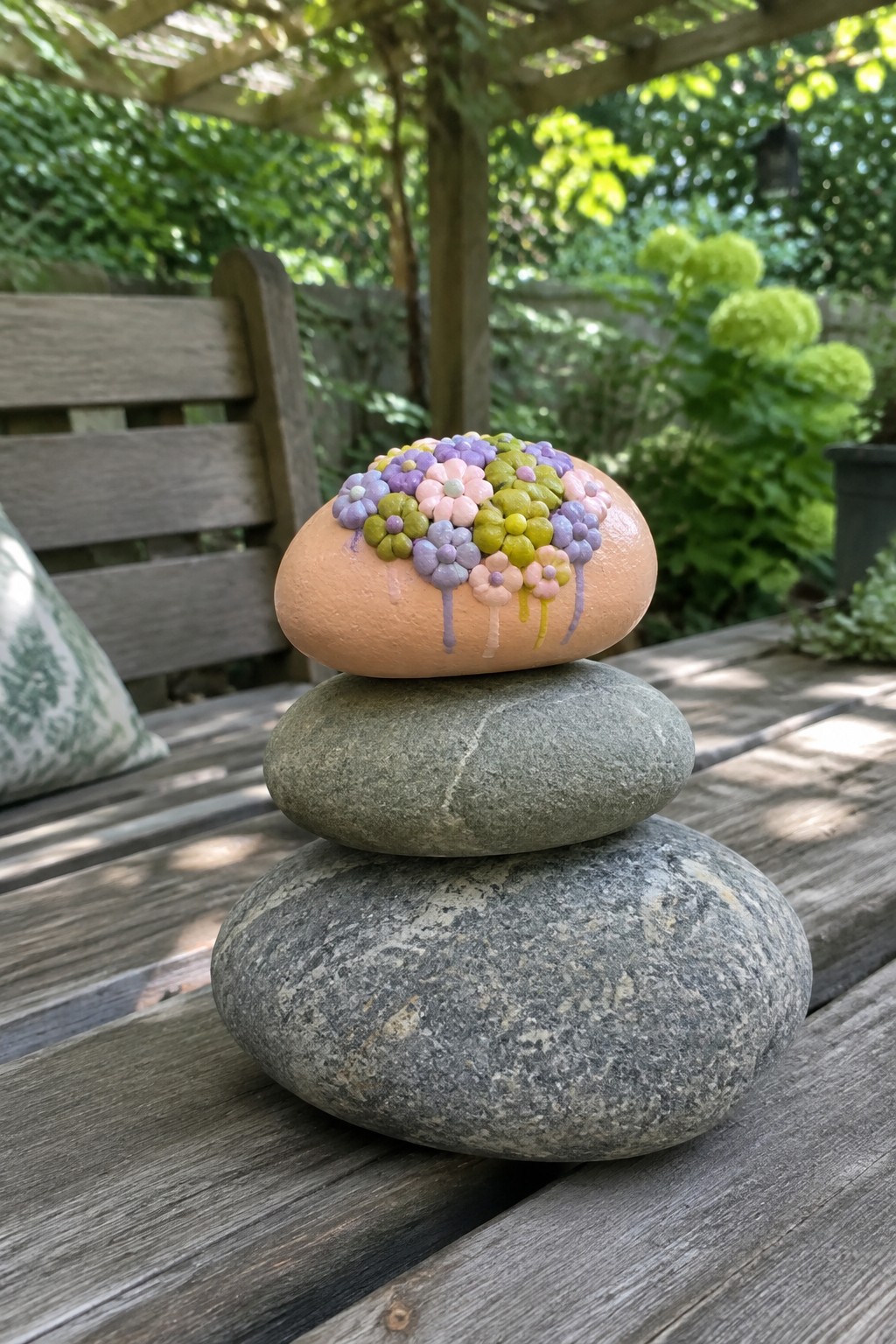 Peach-painted rock with colorful flowers stacked atop two gray stones outdoors