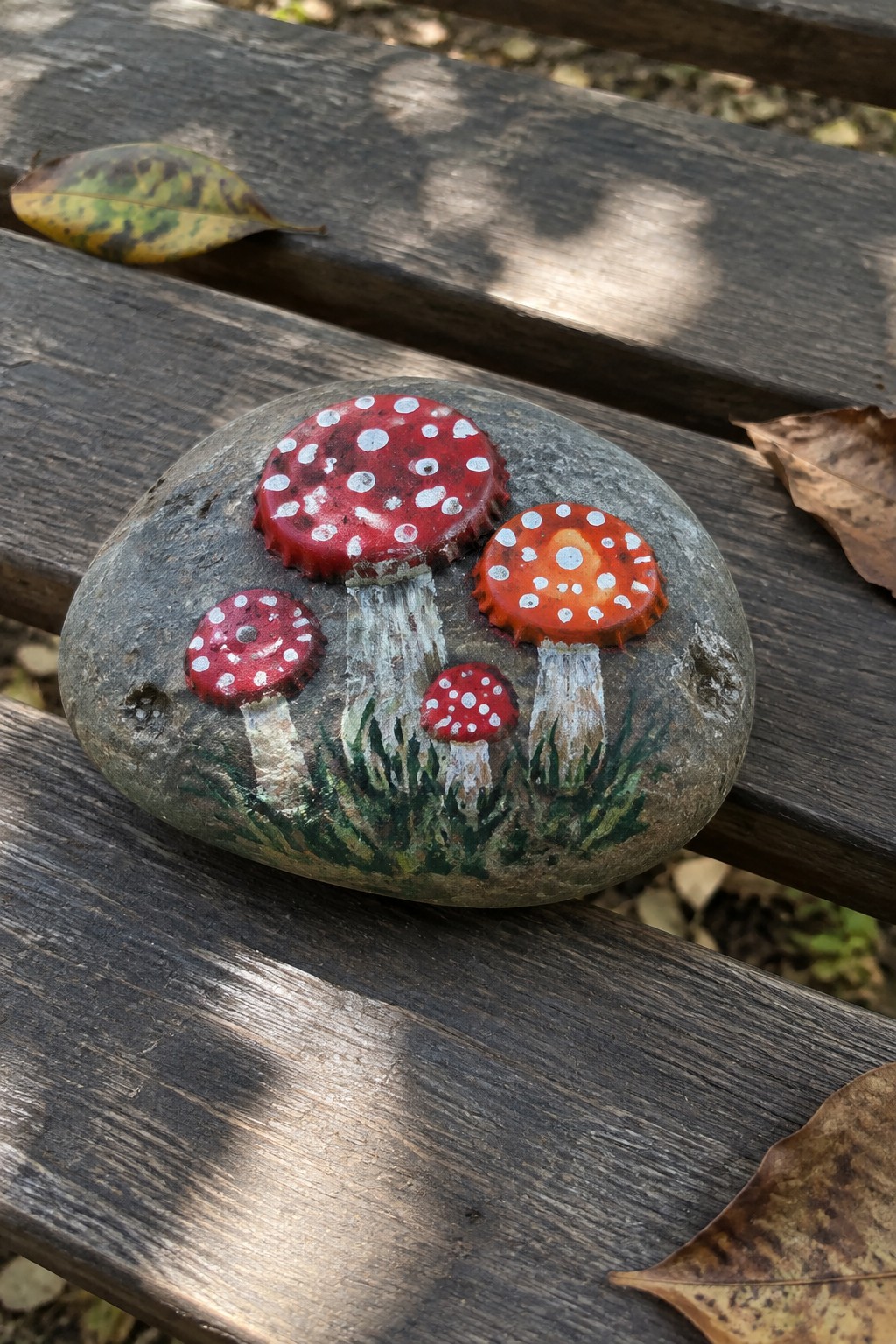 Gray stone on wooden bench painted with red bottle cap mushrooms, white stems, and grass.
