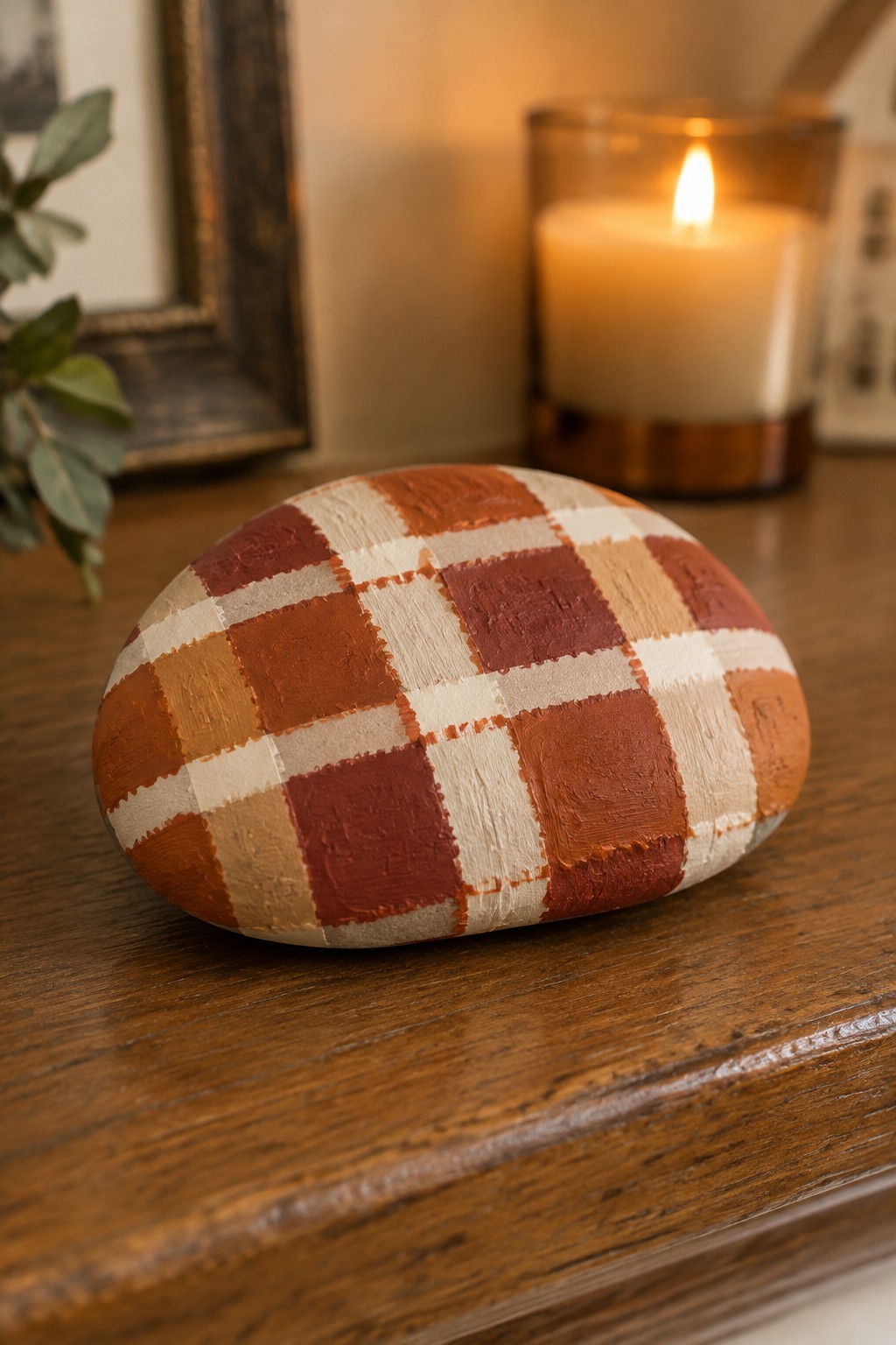 Painted rock with orange-red plaid pattern resting on wooden surface