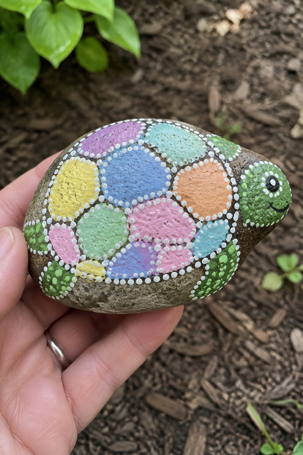 Hand holding colorful painted turtle rock with pastel circular shell in garden.