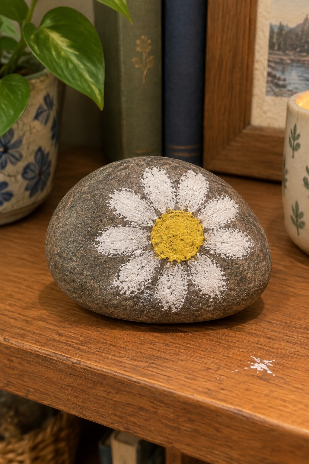 Painted gray rock with white daisy and yellow center on wooden table