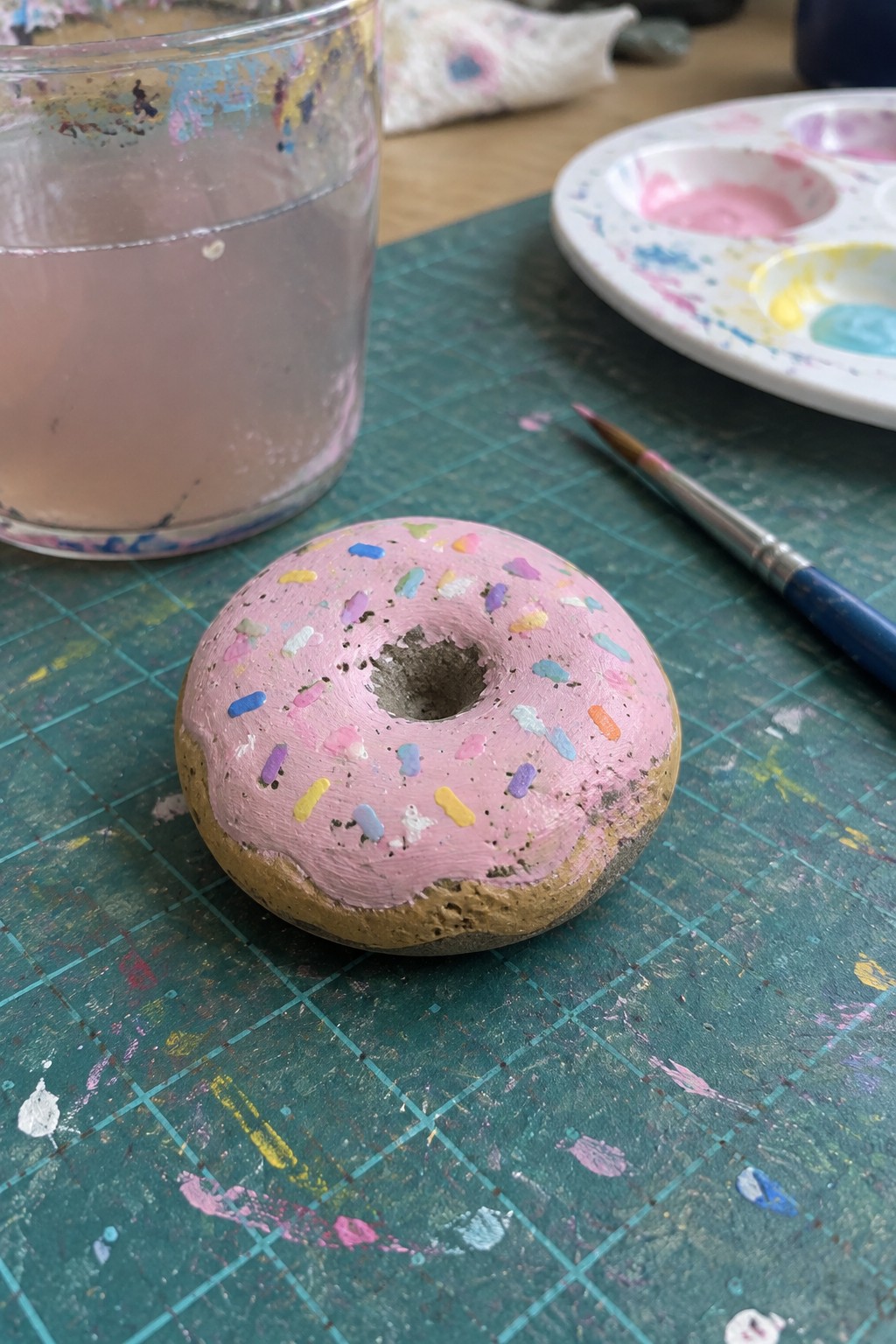 Pink-frosted donut rock with colorful sprinkles on paint-splattered green mat