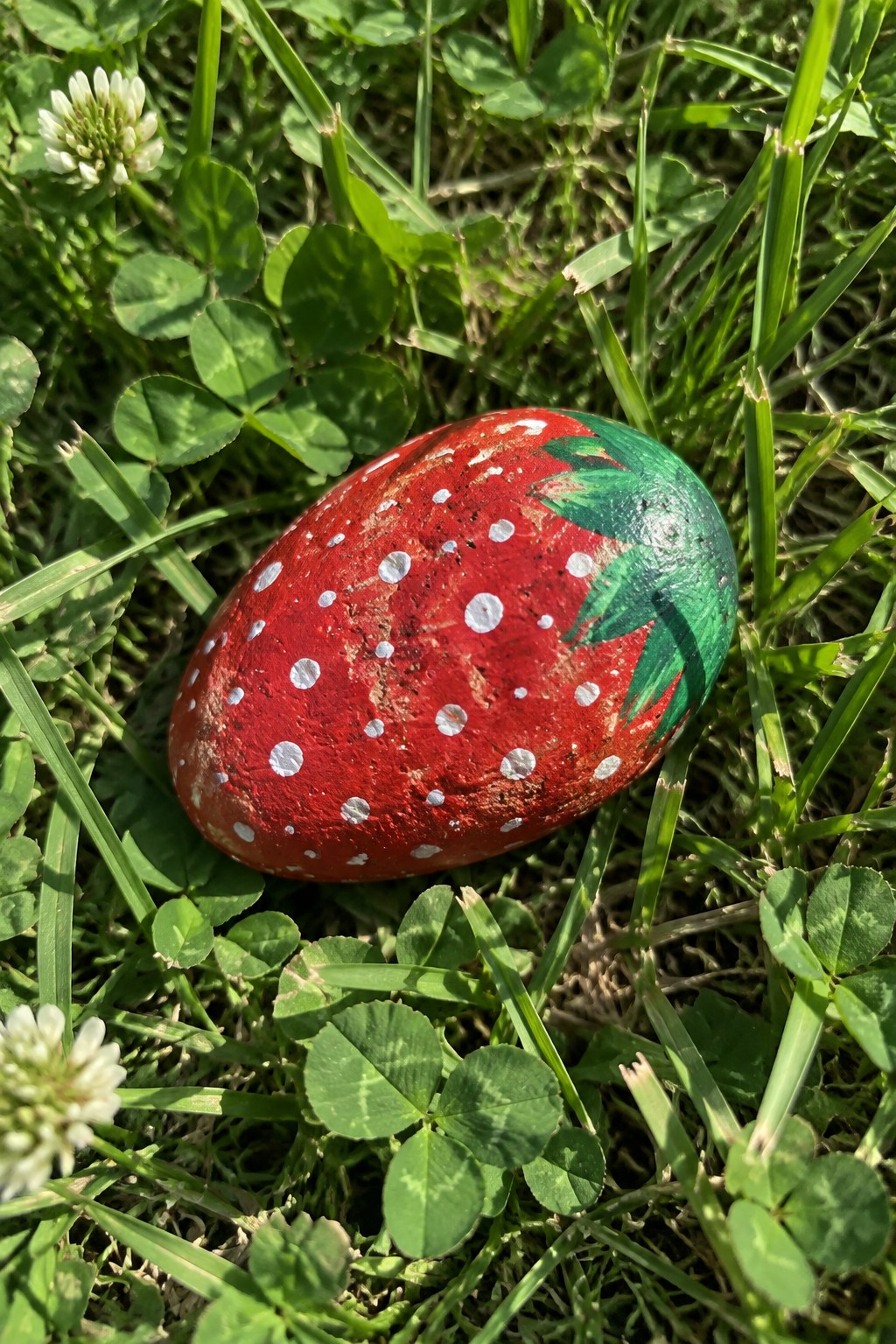 Painted red rock with white dots and green leaves like a strawberry on grass