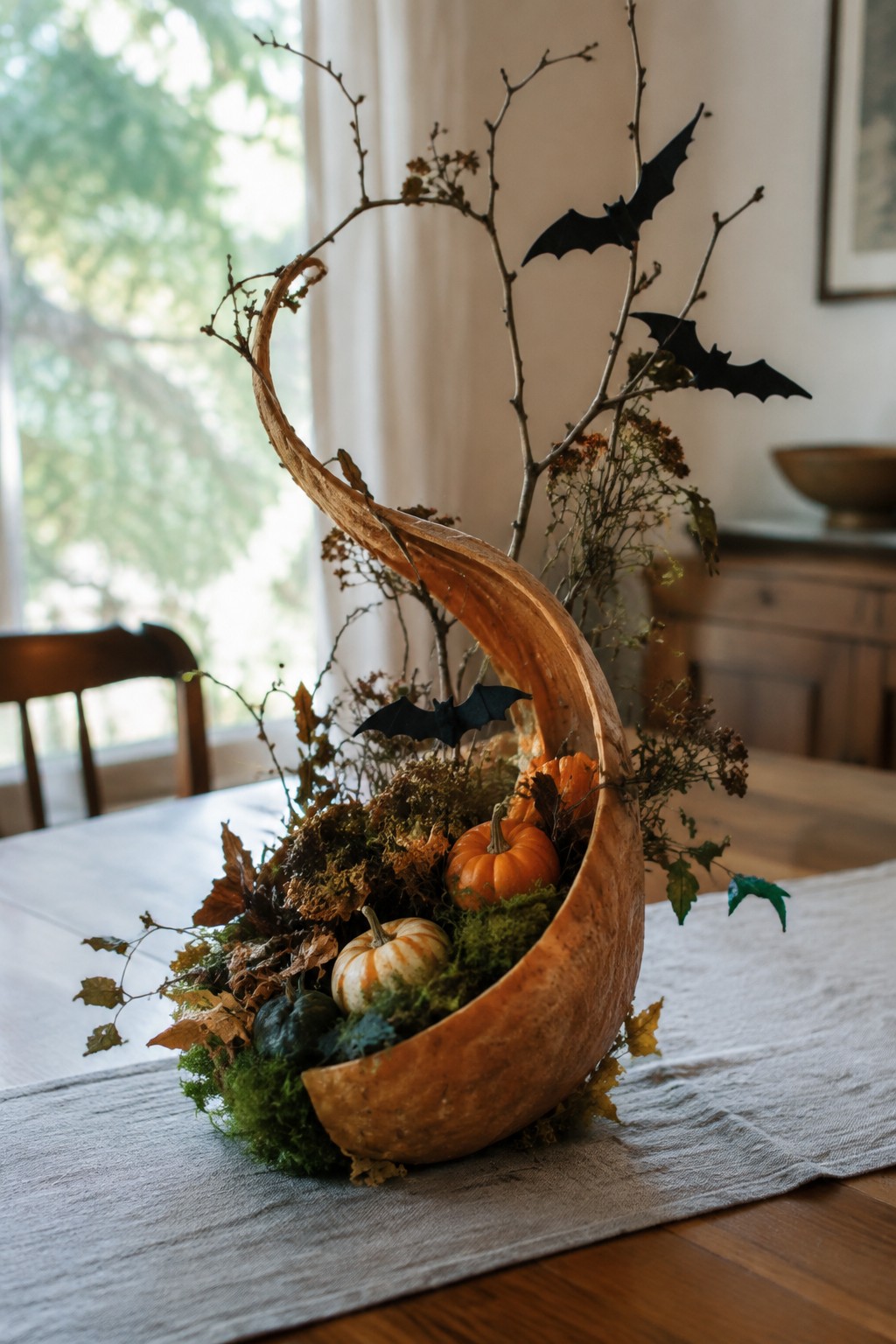 Curved gourd centerpiece with moss, small pumpkins, branches, and black bat decorations on table