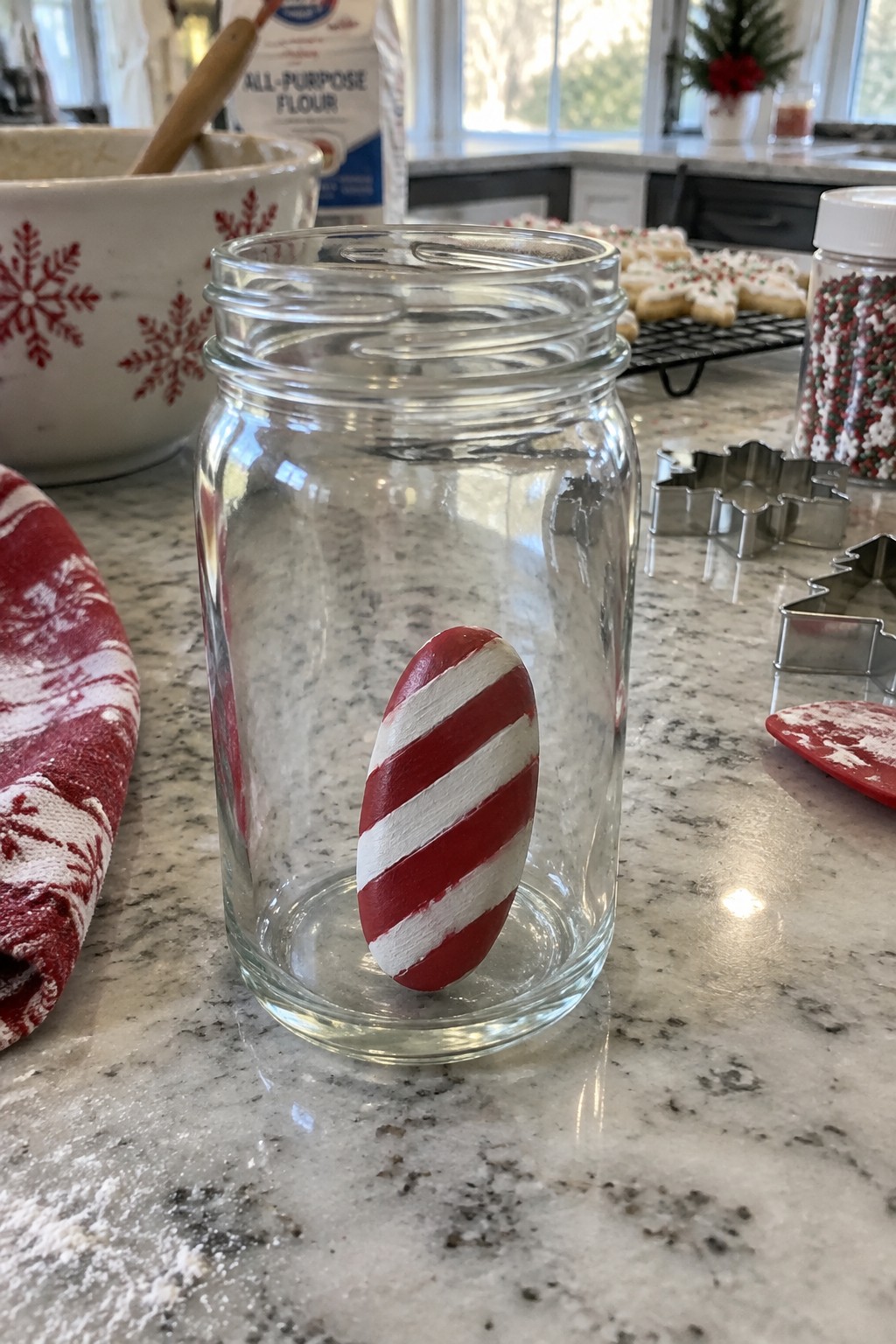 Glass jar with red and white striped egg on marble counter amid holiday baking supplies