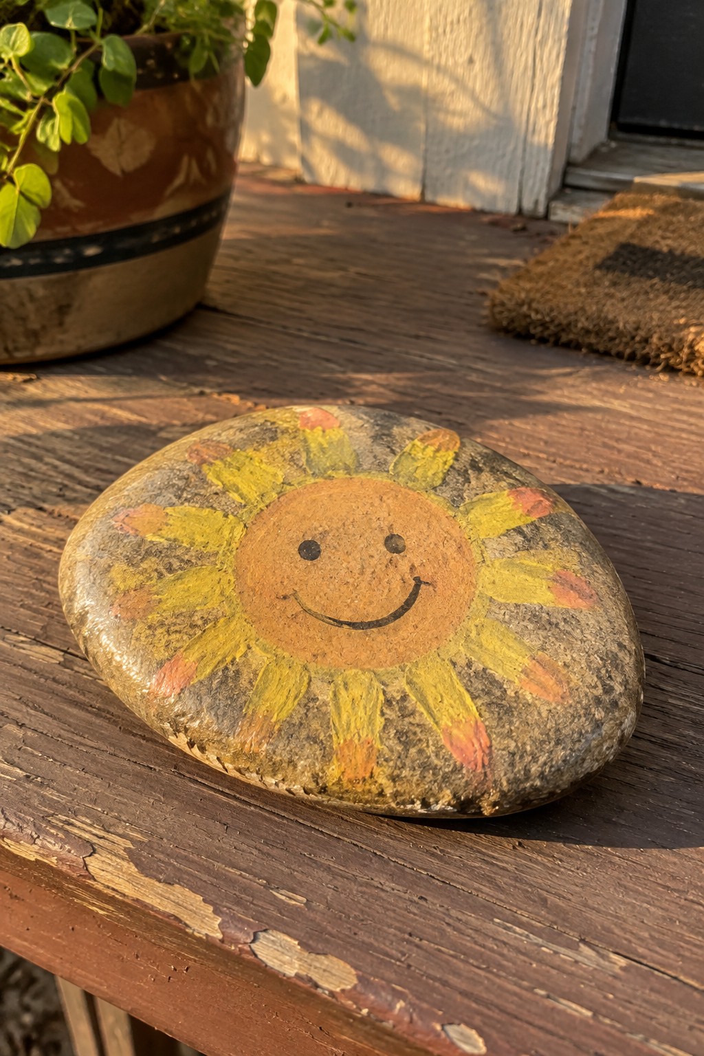 Painted rock with smiling sun face and yellow-orange rays on wooden surface