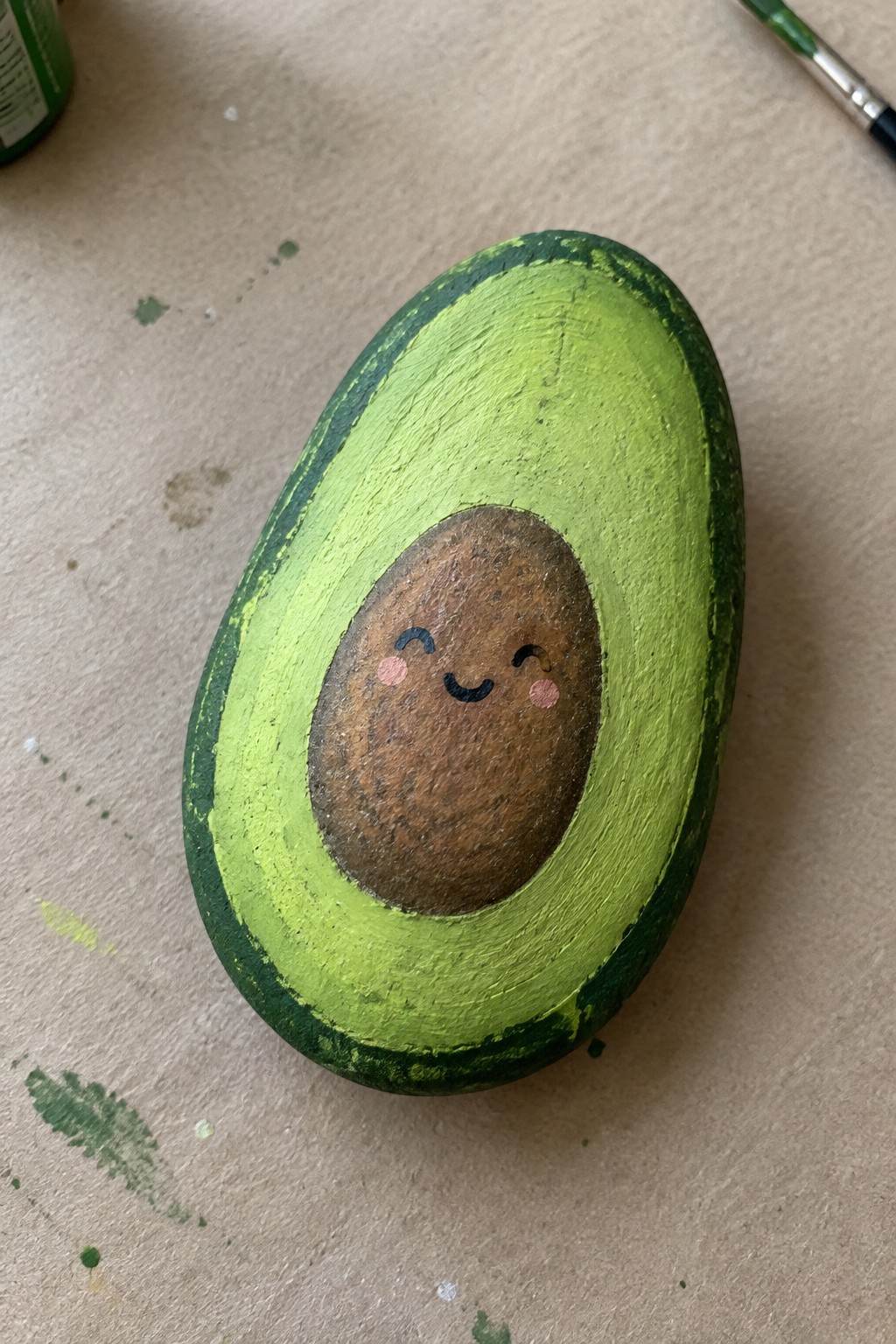 Painted avocado rock with green flesh and cute smiling brown pit on craft table.