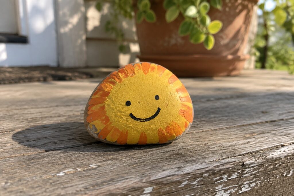 22 Cute Small Rock Painting Ideas Featuring Smiley Faces and Happy Expressions Painted smiling sun rock with yellow face and orange rays on wooden surface