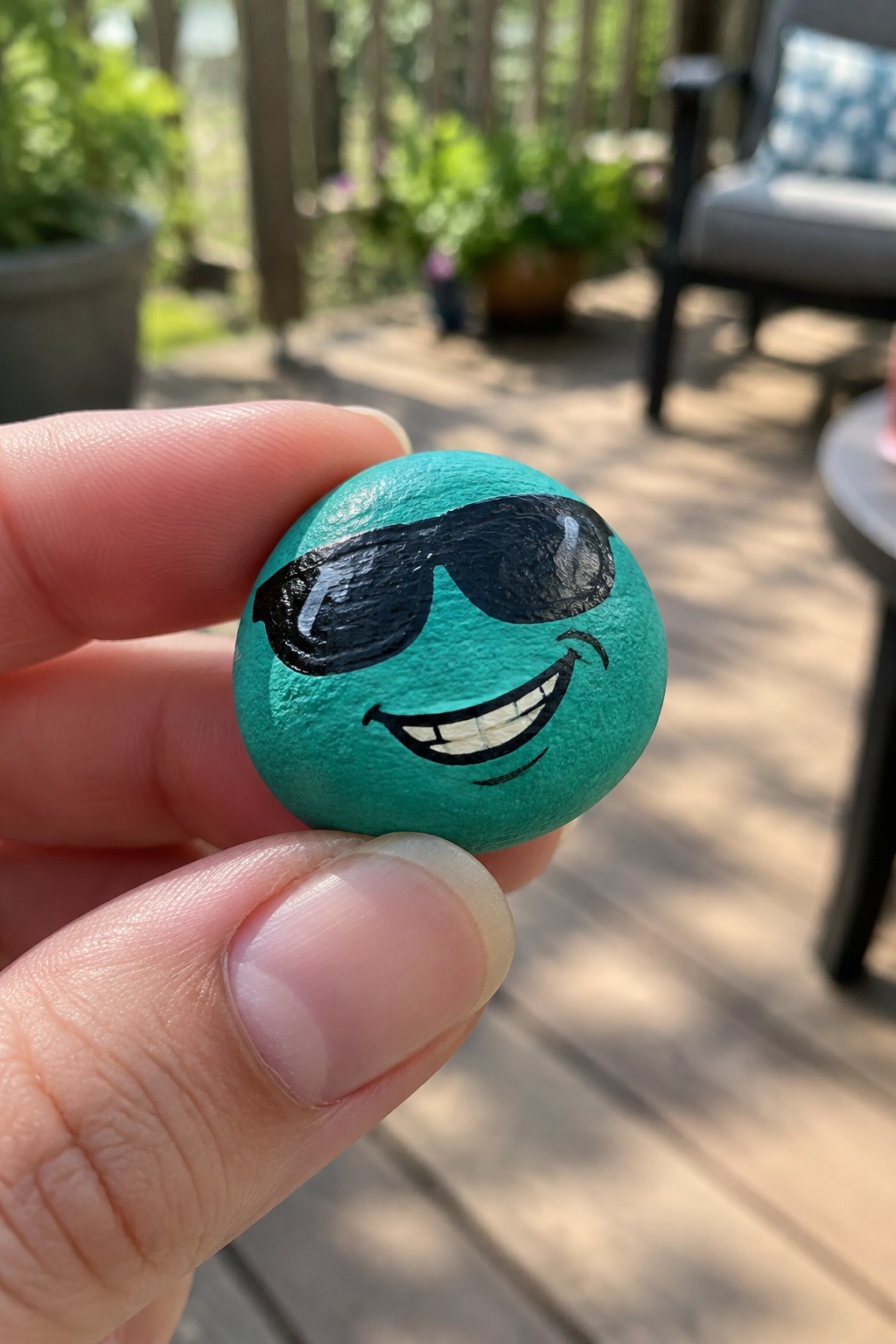 Hand holding small turquoise rock painted with black sunglasses and grin