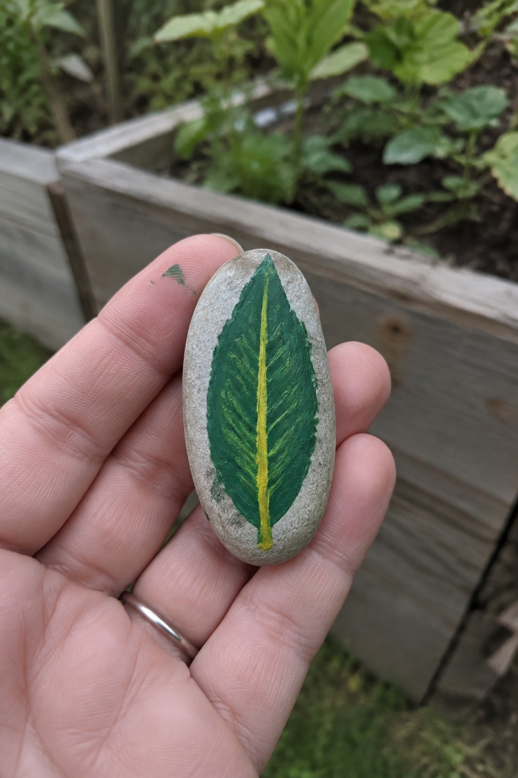 Hand holding oval gray stone painted with green leaf and yellow vein