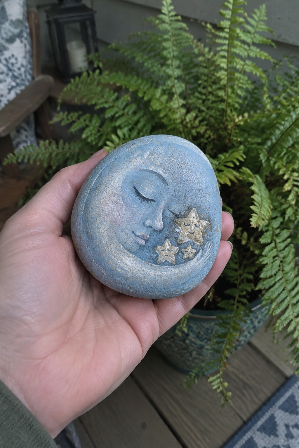 Hand holding blue painted stone with moon face and three stars
