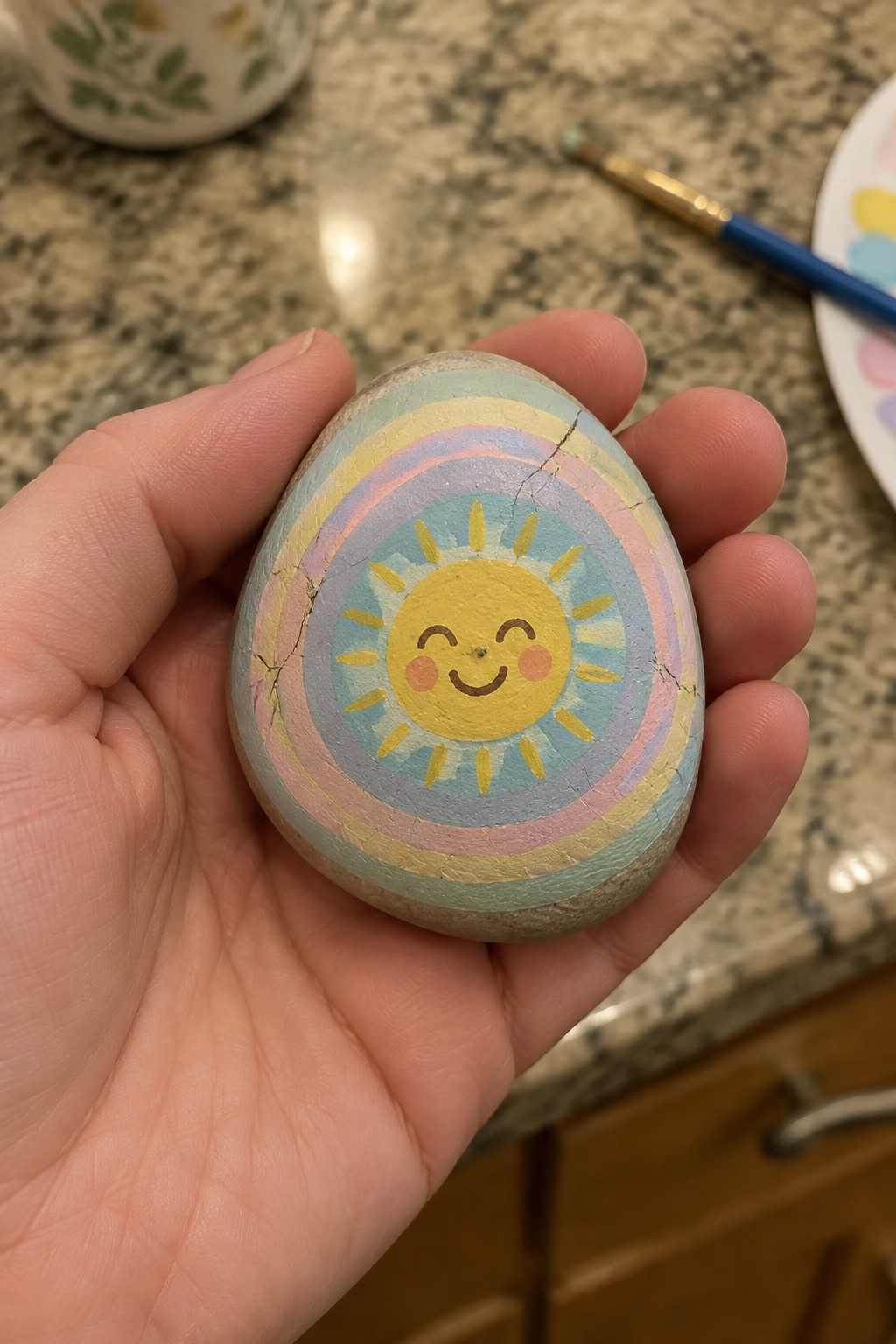 Hand holding cracked pastel rainbow rock with smiling yellow sun face