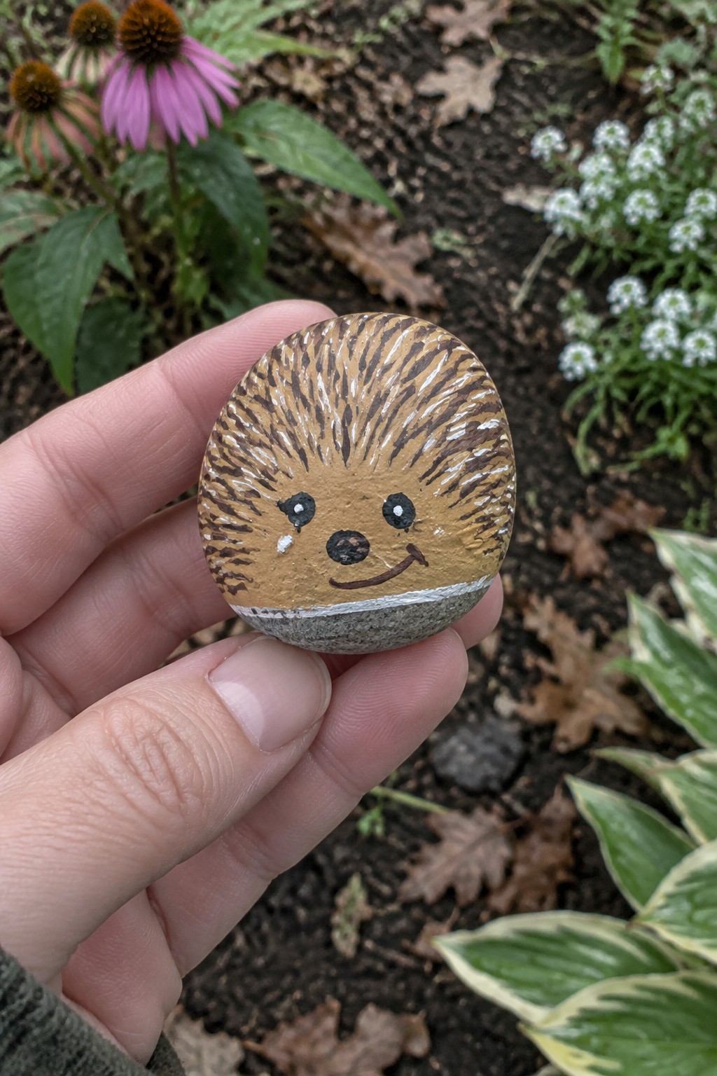 Hand holding a smiling hedgehog rock painted brown with spiky stripes in garden