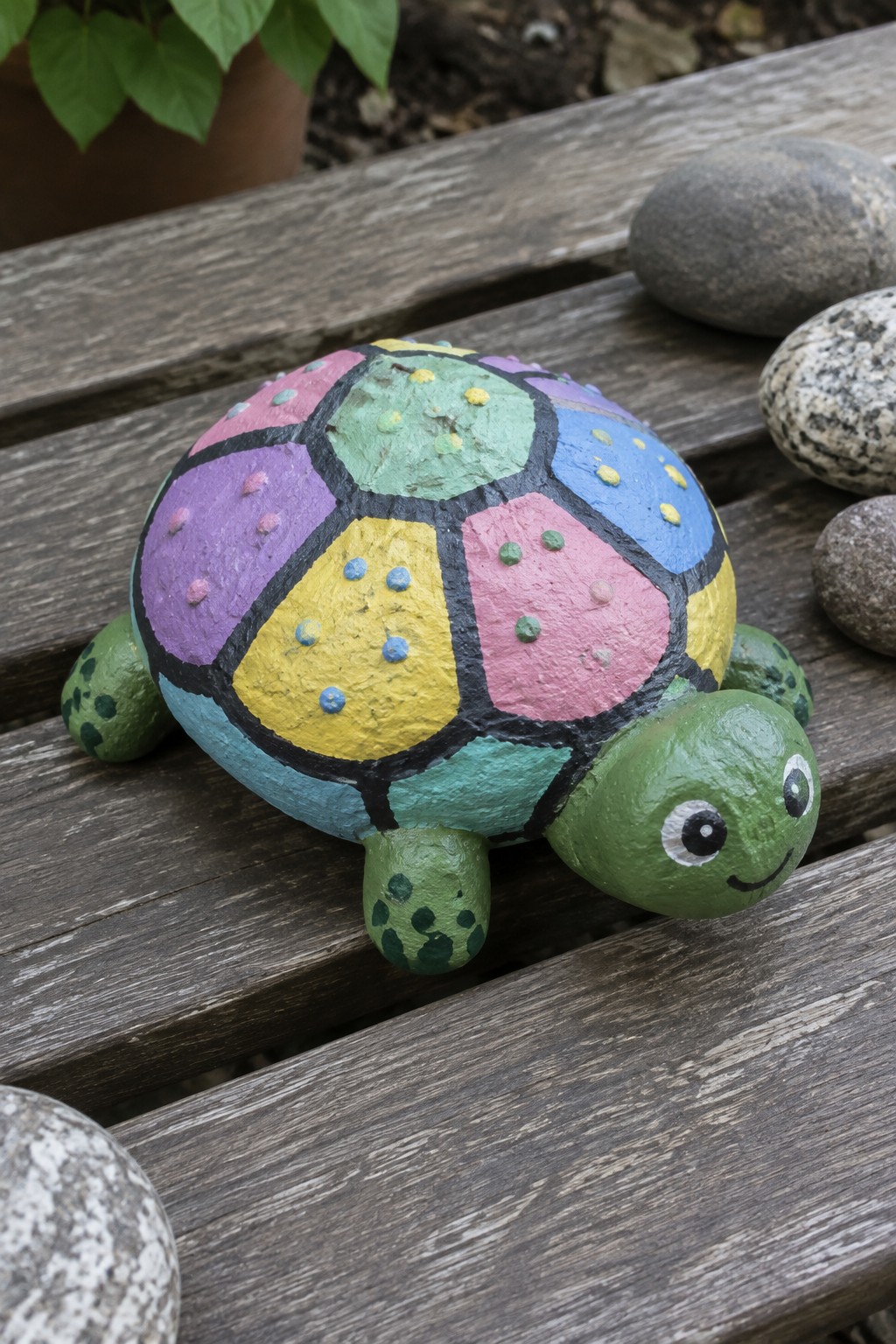 Colorful painted turtle rock with patchwork shell on wooden planks beside stones