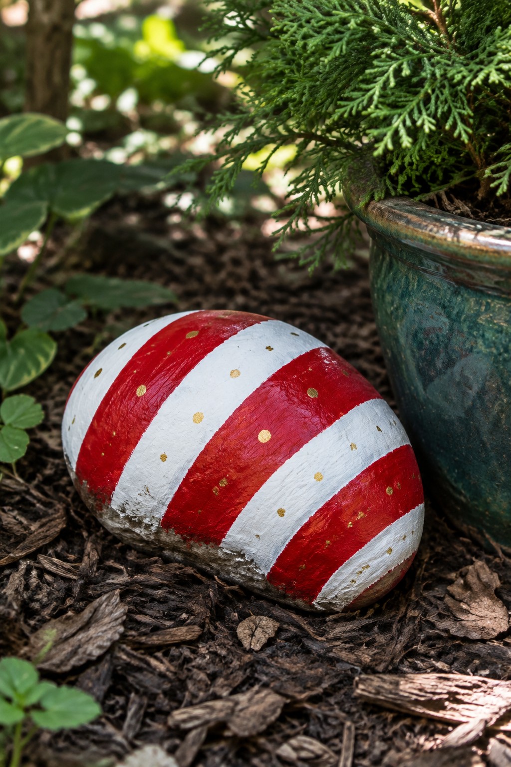 Red and white striped painted rock with gold dots beside potted plant