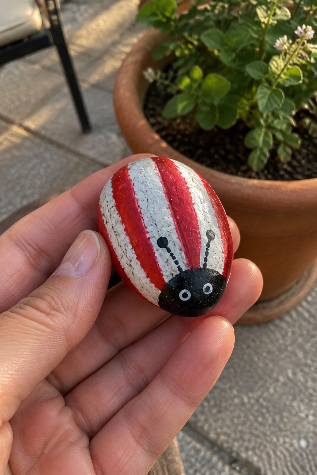 Hand holding red-and-white striped ladybug rock with black head and antennae.