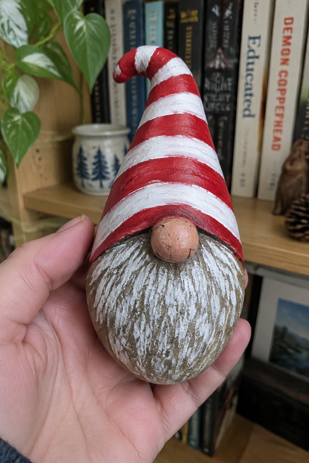 Hand holding red-and-white striped gnome figurine with brown textured body and nose