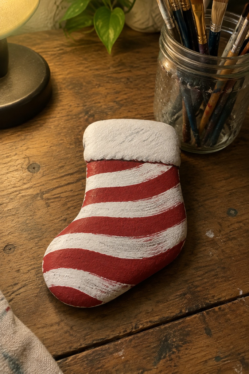Red and white striped Christmas stocking painted on rock atop wooden table