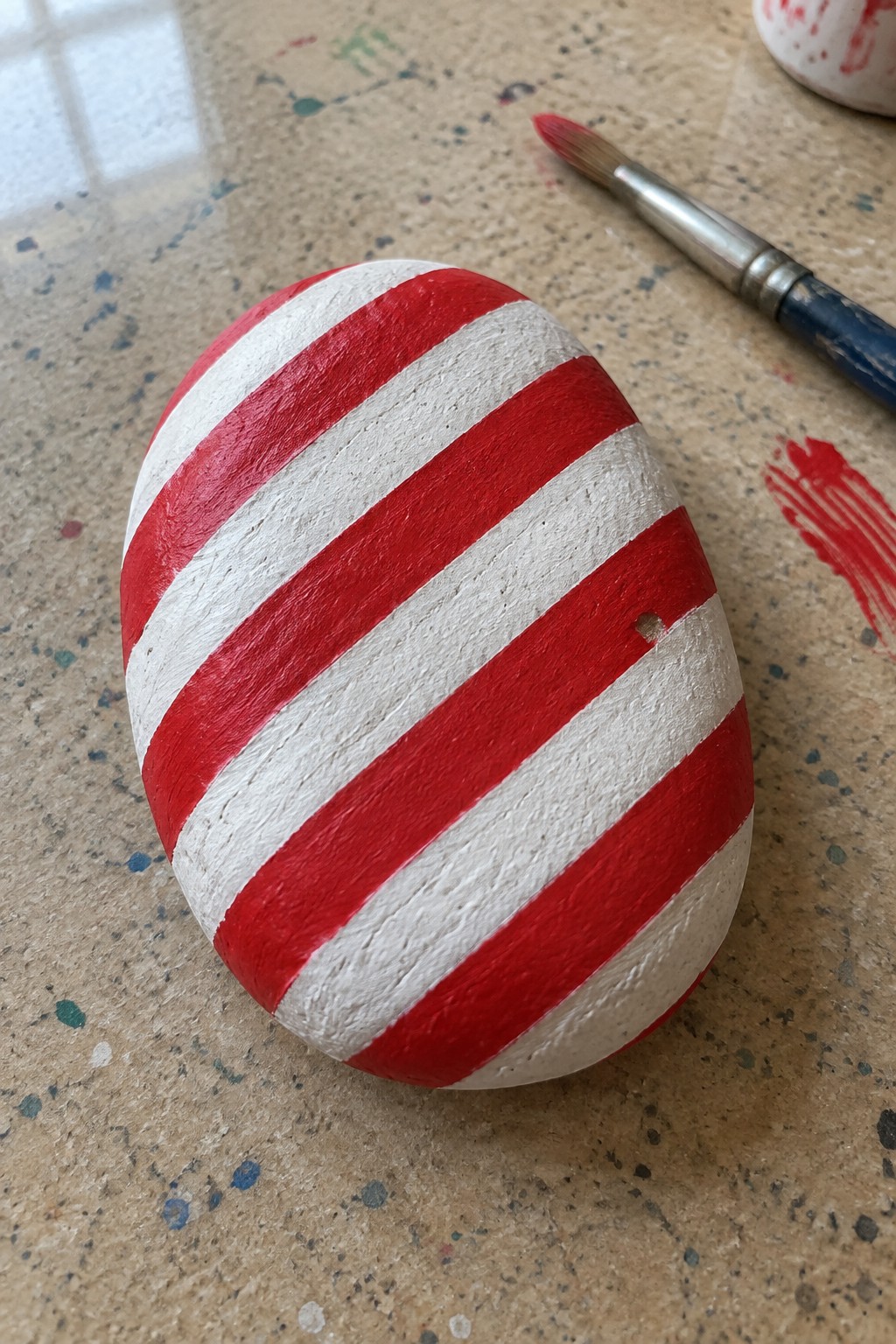 Red and white striped painted rock beside paintbrush on speckled surface