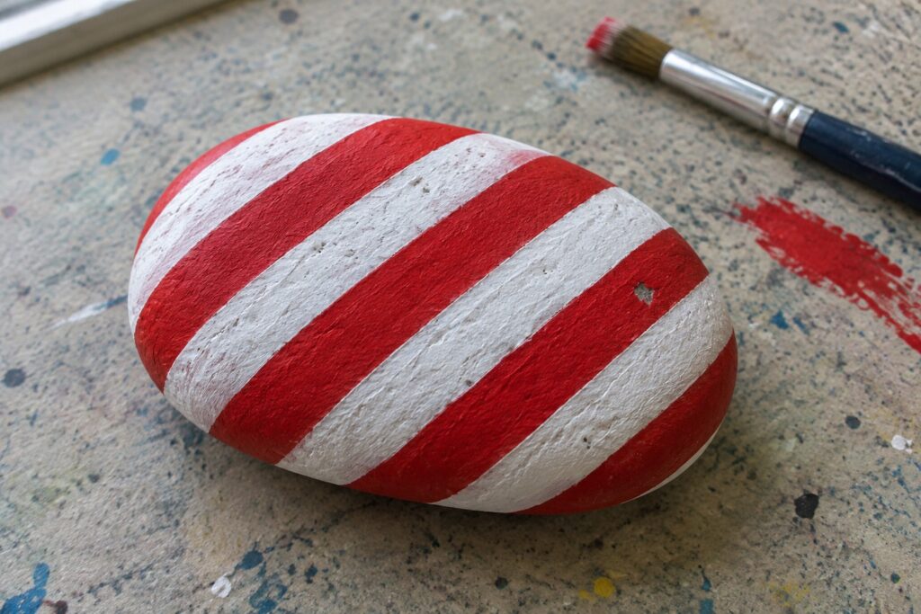 Red and white striped painted rock beside paintbrush on speckled surface