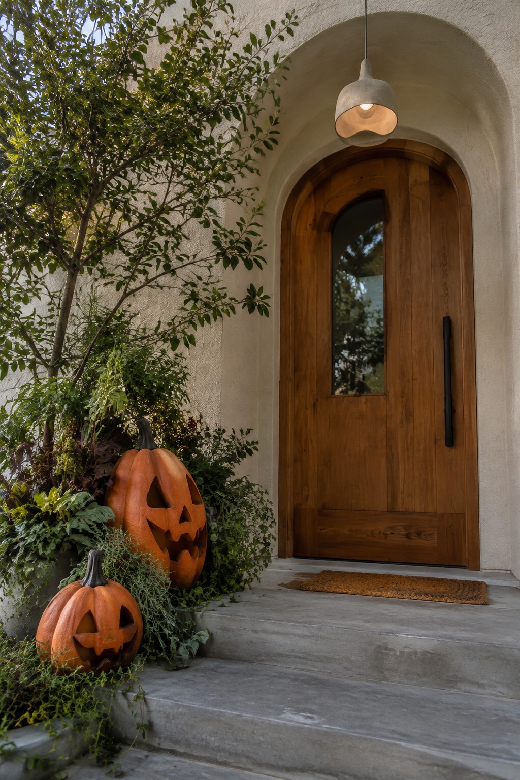Two carved pumpkins beside arched wooden door on concrete steps with plants