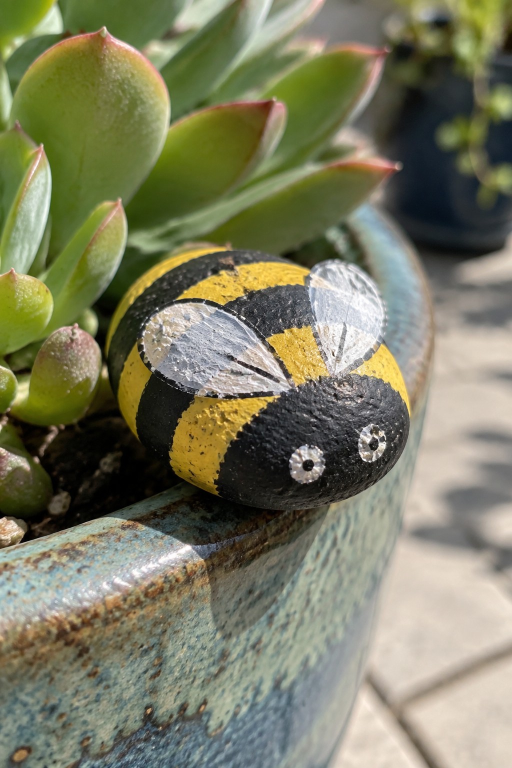 Yellow and black striped bumblebee rock with wings in succulent-filled blue pot