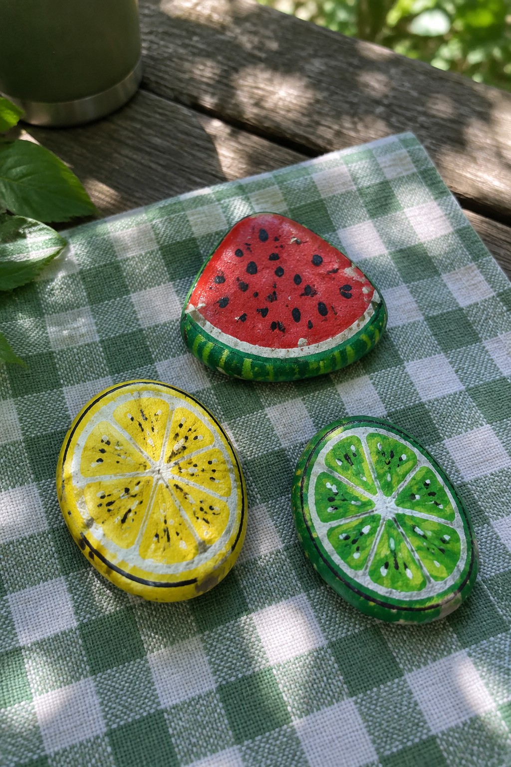 Three painted rocks as watermelon, lemon, and lime on green checkered cloth.