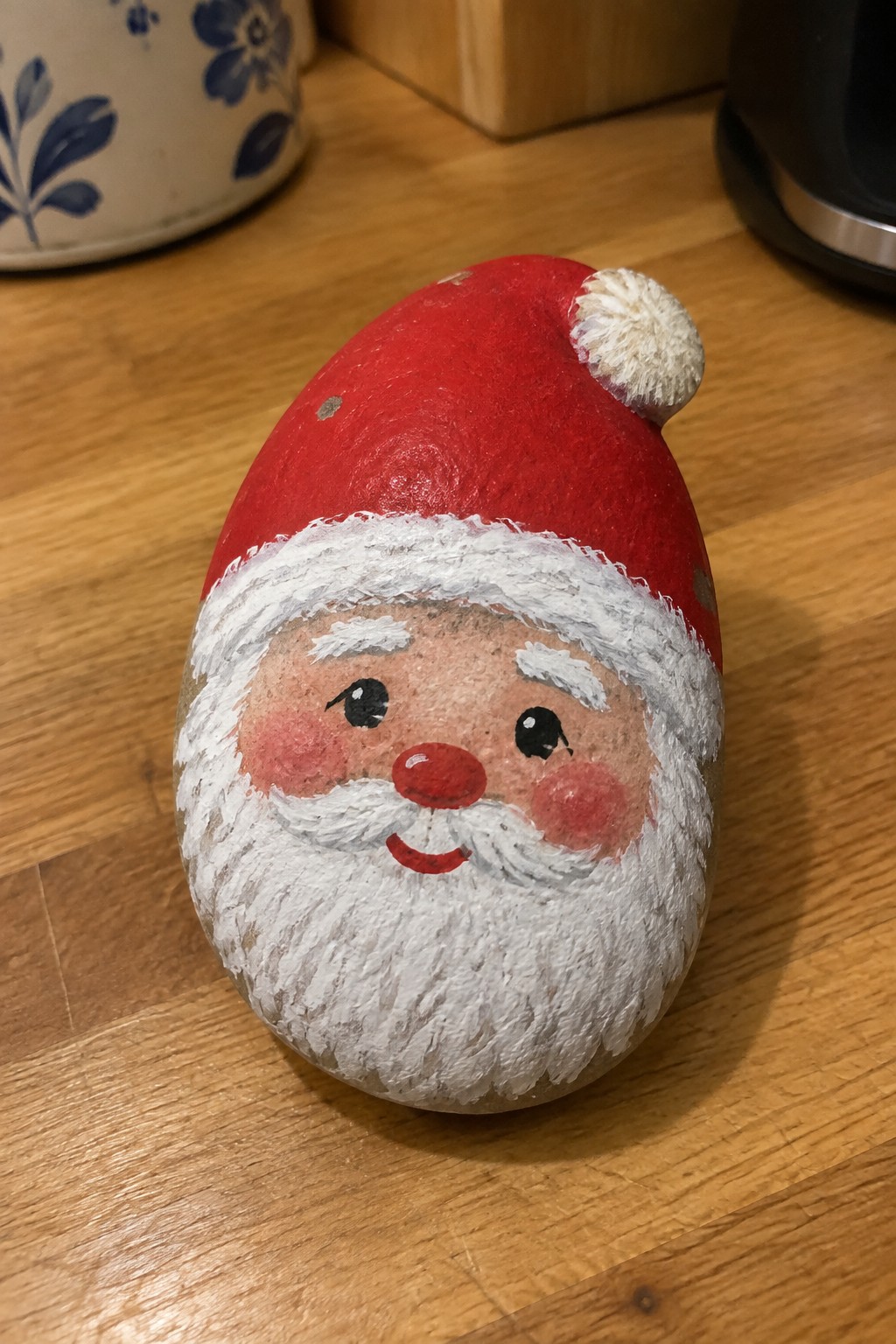 Painted rock shaped as Santa with red hat, white beard, and rosy cheeks.