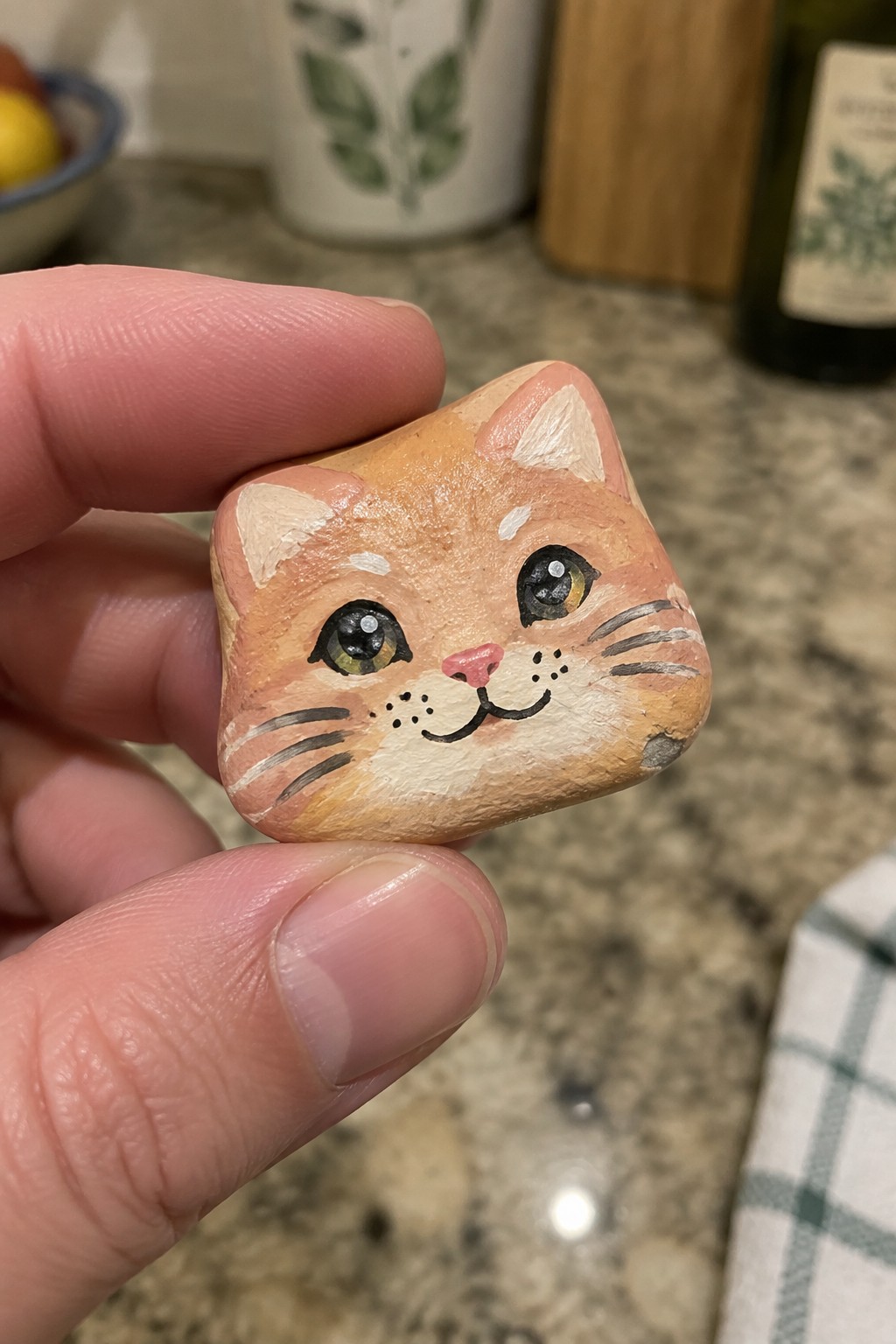 Hand holding small painted rock shaped as orange cat face with big eyes