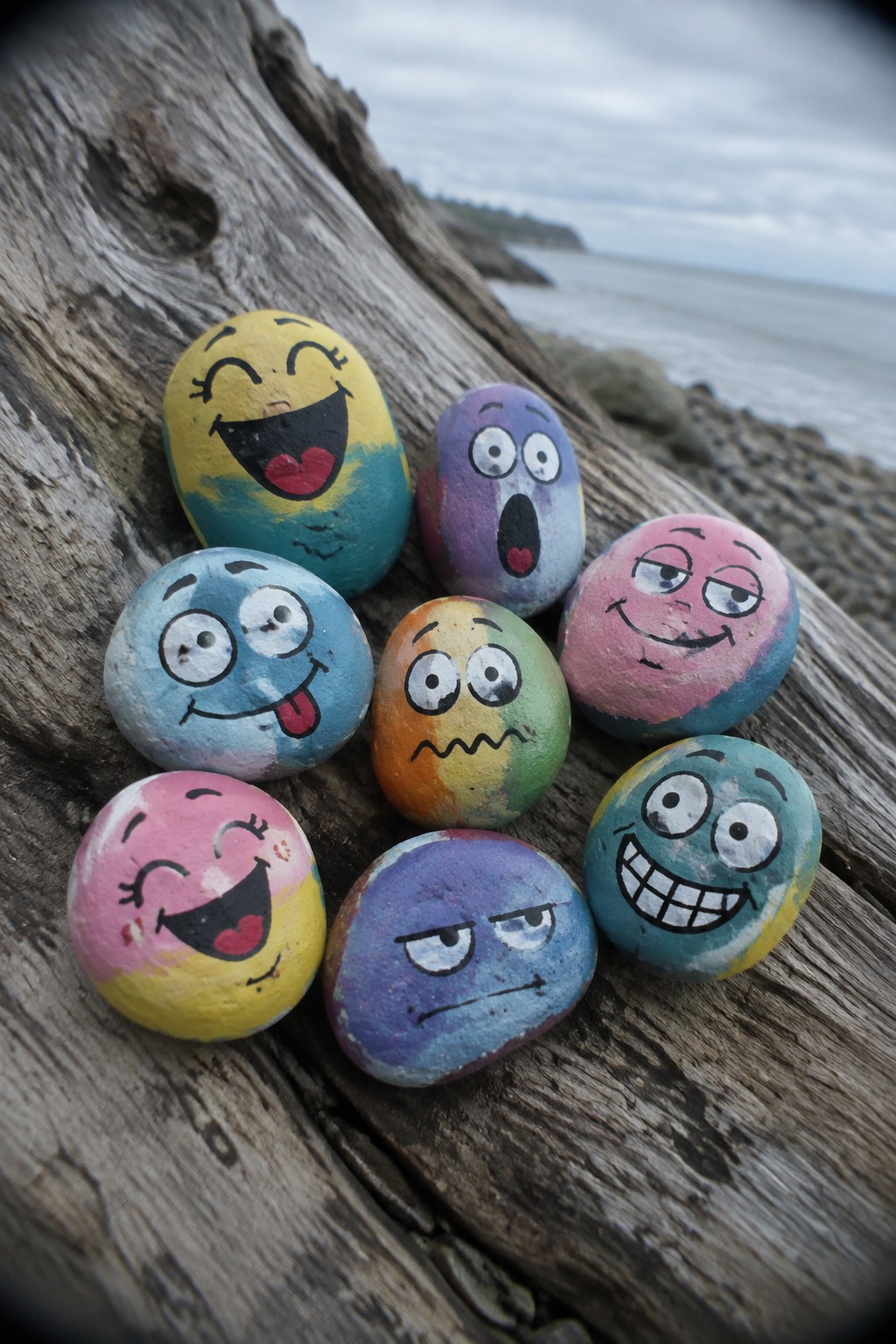 Colorful painted rocks with cartoon faces on driftwood by the ocean